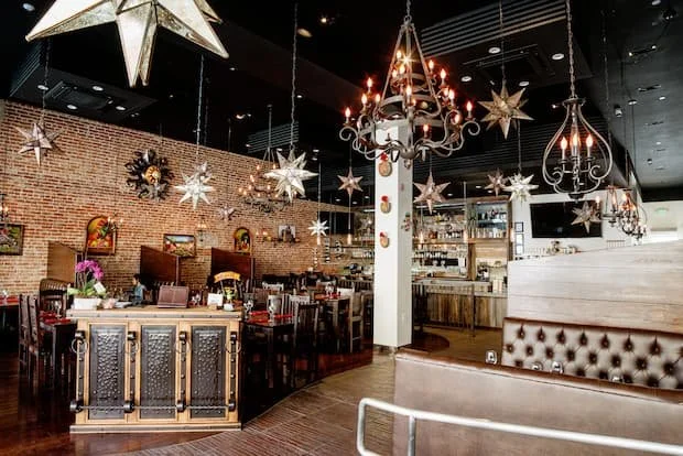 Interior of a decorated restaurant with hanging star-shaped and chandelier lights, a brick wall, dining tables, and a bar area.