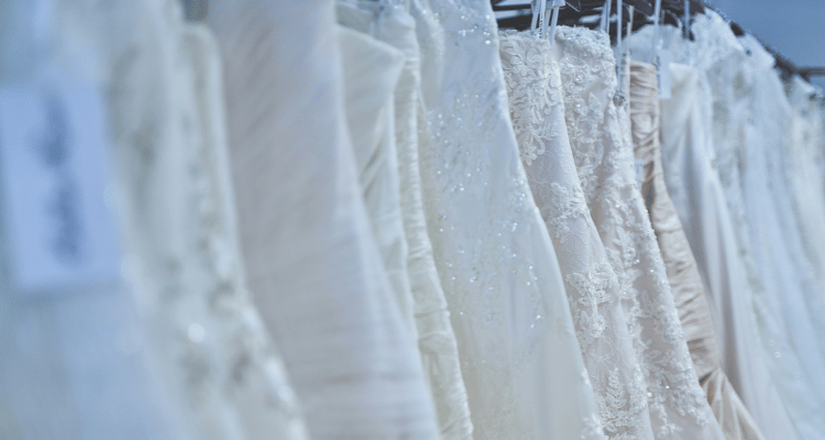 A row of elegant white wedding dresses on hangers, showcasing various lace and satin textures, conveying a sense of romance and anticipation.