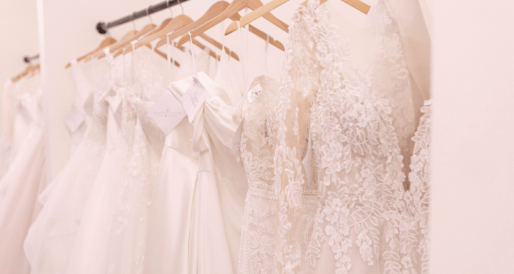 A row of elegant white wedding dresses on wooden hangers, featuring intricate lace and tulle, creates a serene and romantic bridal atmosphere.