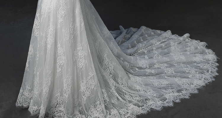 Wedding dress with a lace train extending across a dark floor.