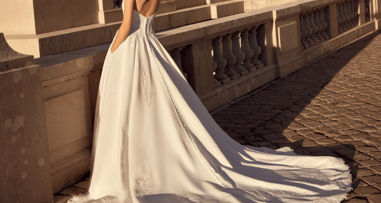 Bride wearing a ball gown wedding dress with an extended train on a sunlit stone walkway.