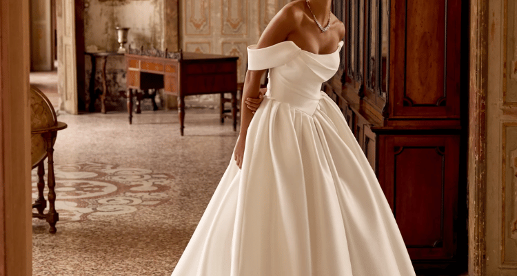 Bride wearing one of the elegant minimalist wedding dresses with an off-the-shoulder neckline and full satin skirt.