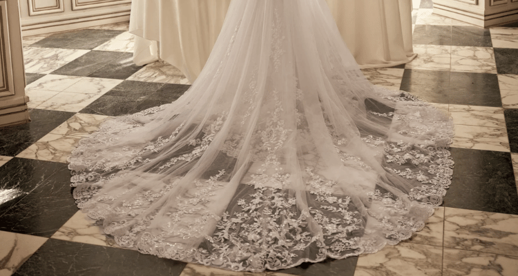 Wedding dress with a long lace train spread across a black and white marble floor.