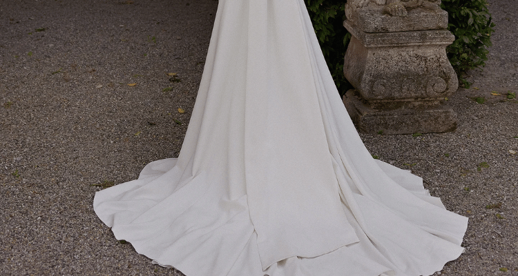Bride wearing a simple wedding dress with a flowing train on a gravel path.