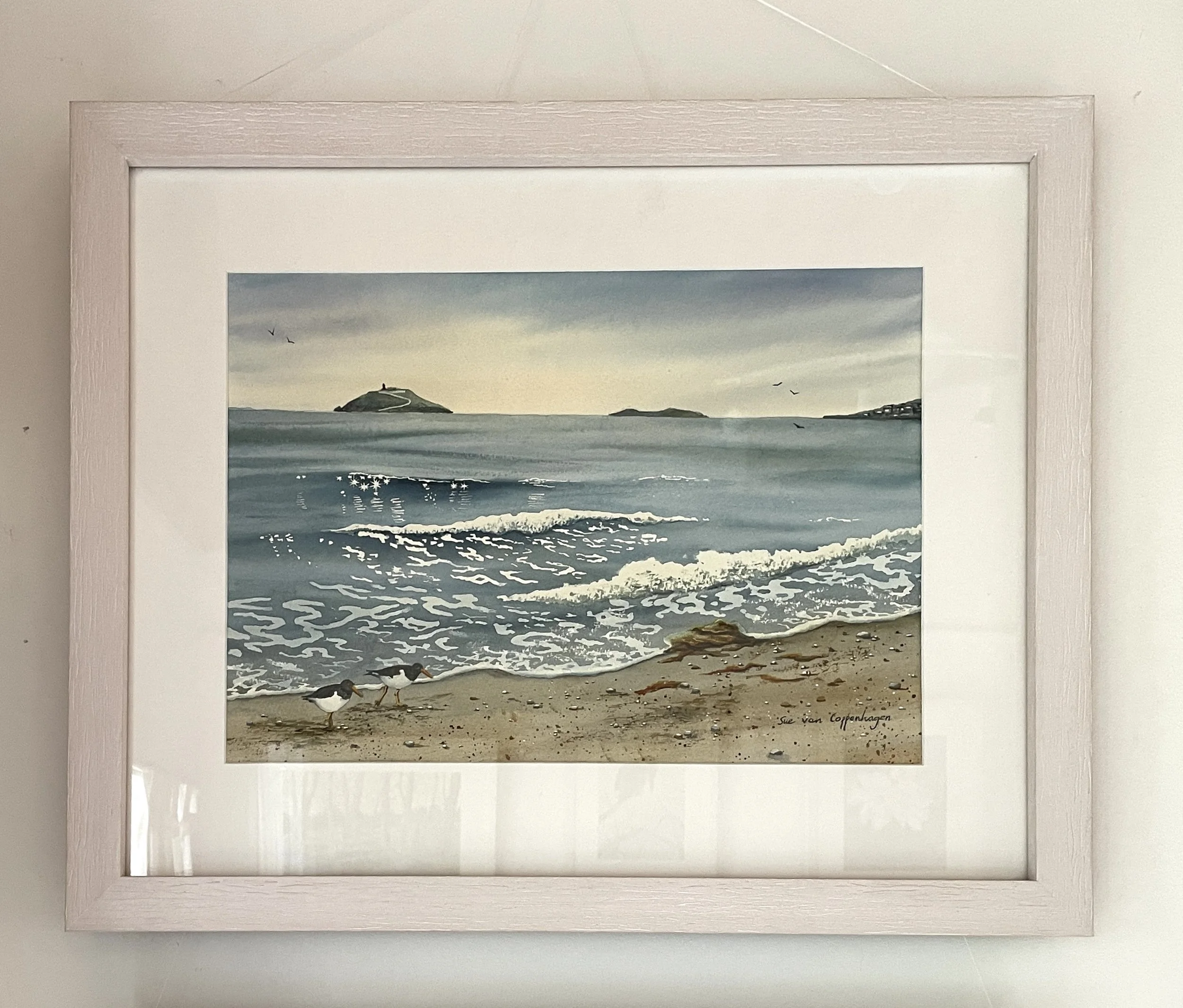 Framed seascape painting of Ballycotton Bay, showing waves lapping on the beach with two oystercatcher birds and Ballycotton island on the horizon
