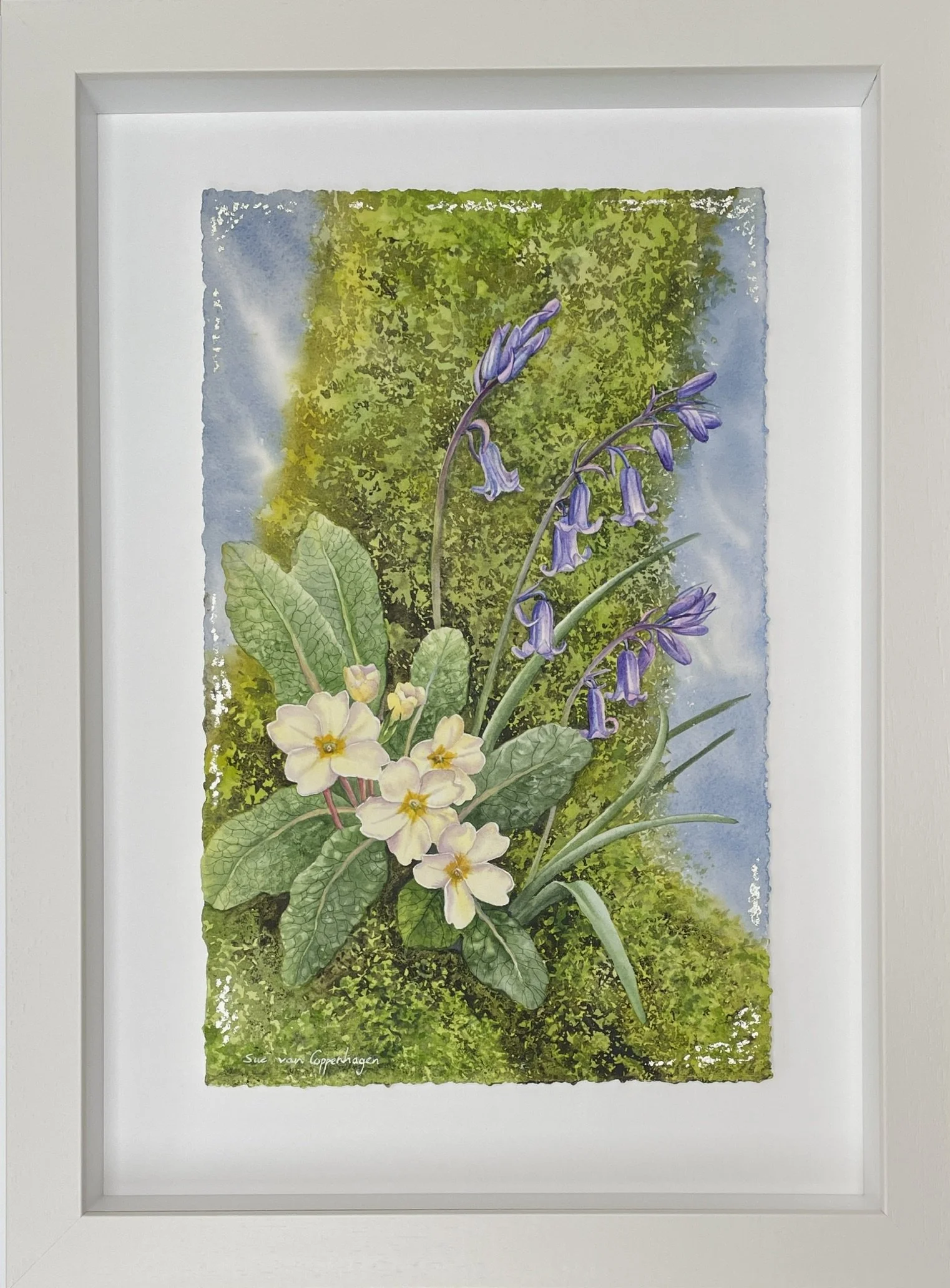 Framed painting of yellow primrose flowers and bluebells beneath a moss-covered tree