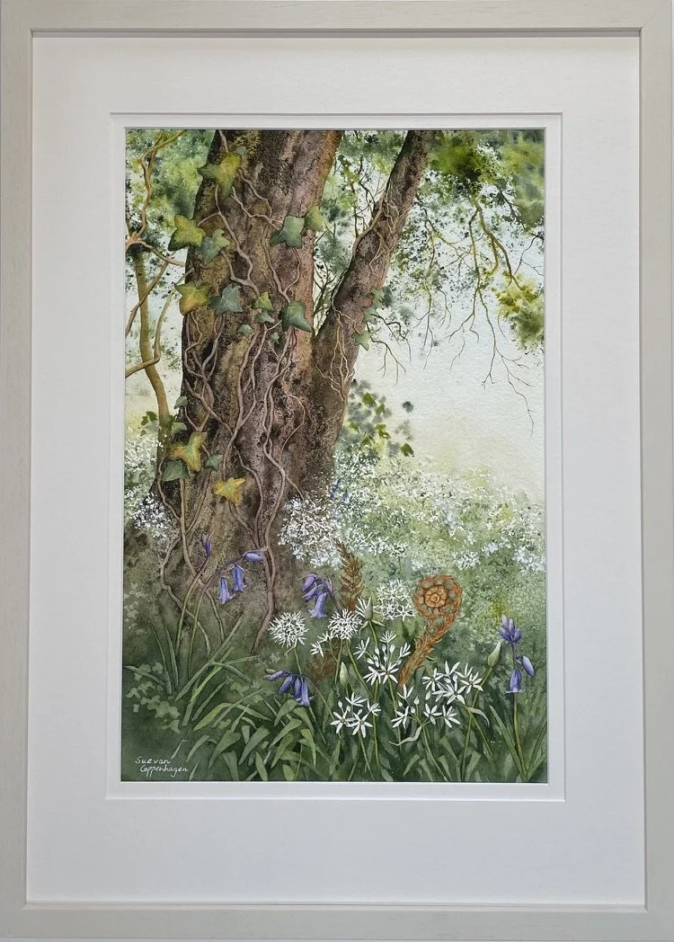 Painting in an off-white frame of a tree in Spring leaf above white wild garlic flowers, bluebells and an unfurling fern