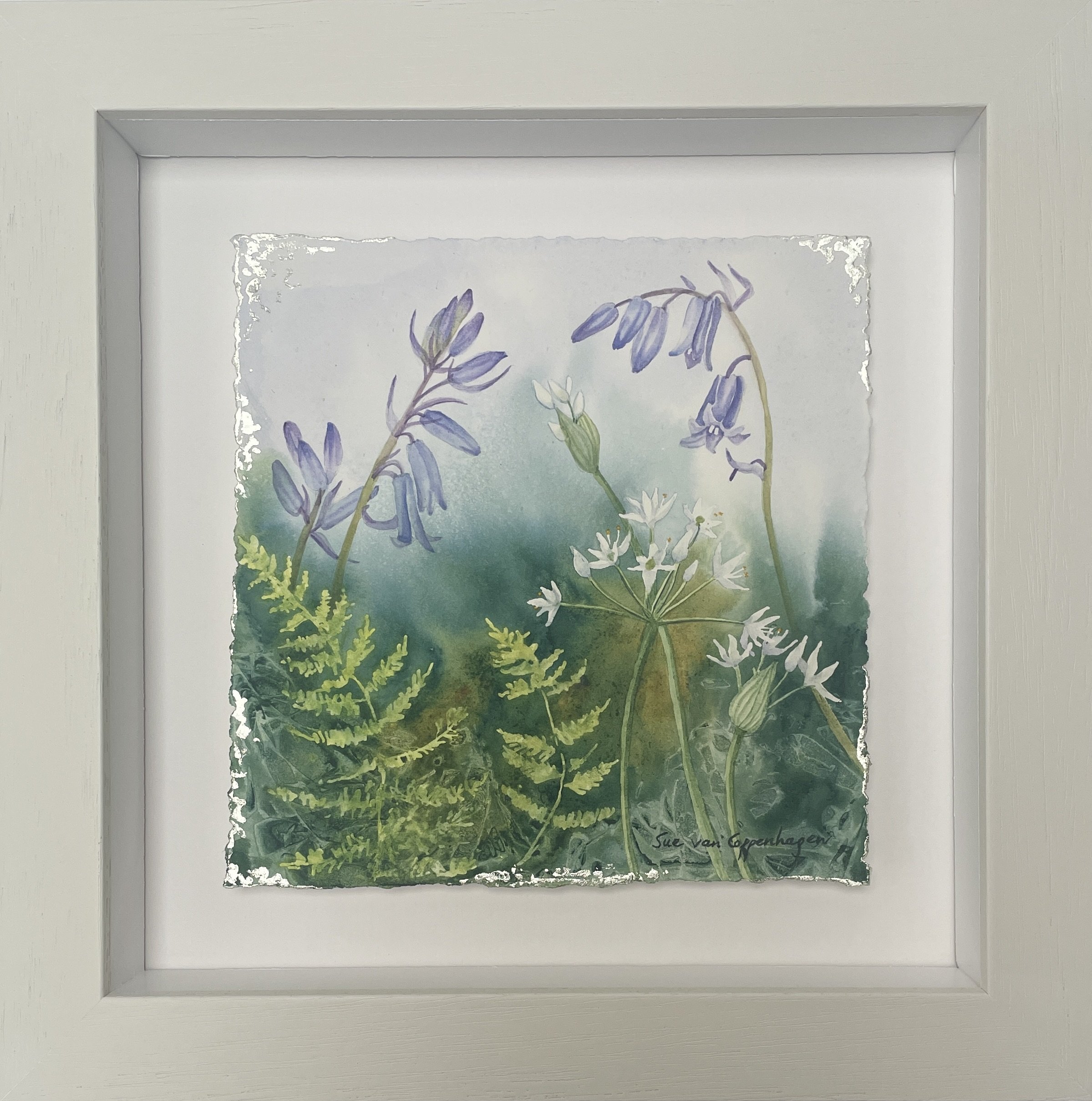 Painting of bluebells, white ramsons and bright green ferns against a blue background above and dark green below, framed in an off white square frame