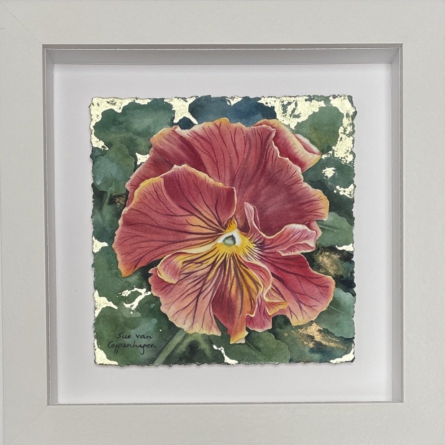 Painting of a frilly purple pansy on a green background with gold leaf, framed in an off white wooden frame