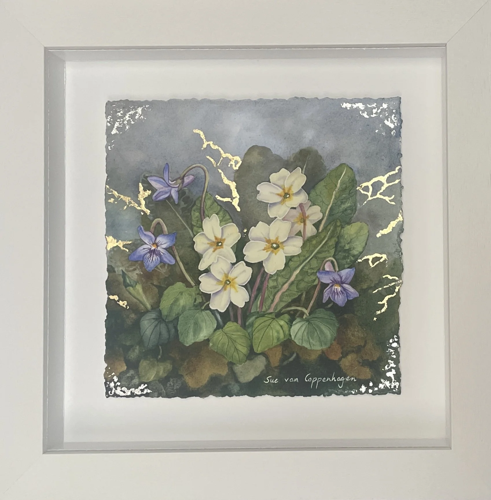 Watercolour painting of three violet flowers and five pale yellow primroses in a wide off-white frame