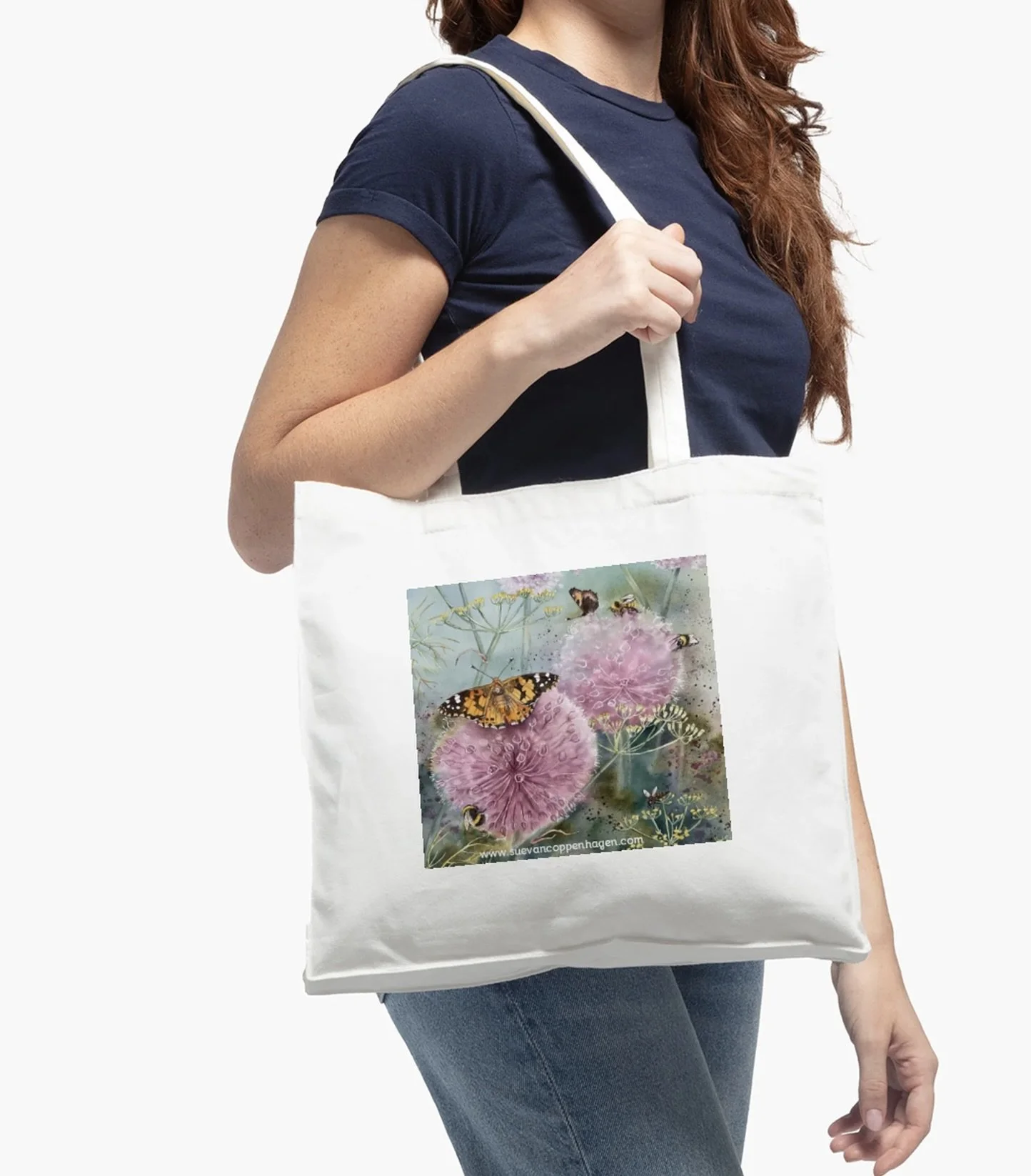 Woman in blue clothes modelling a white cotton tote bag with an image of a Painted Lady butterfly on pink allium flowers