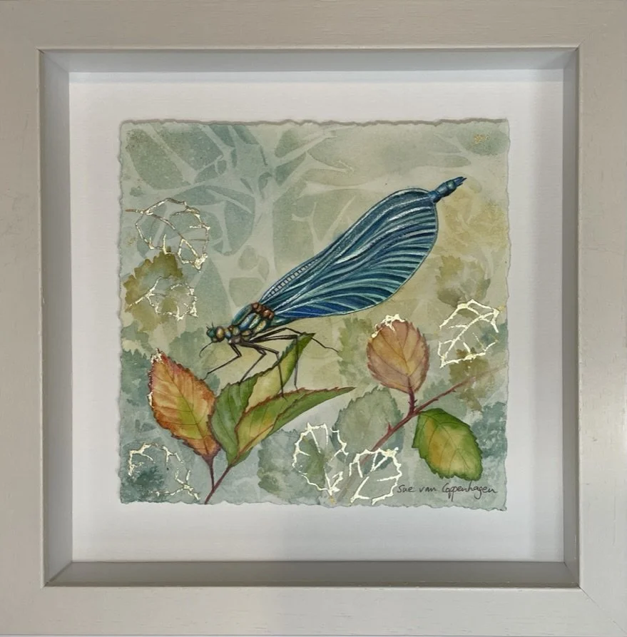 Framed watercolour of a blue damselfly with gold leaf patterns of leaves in the background