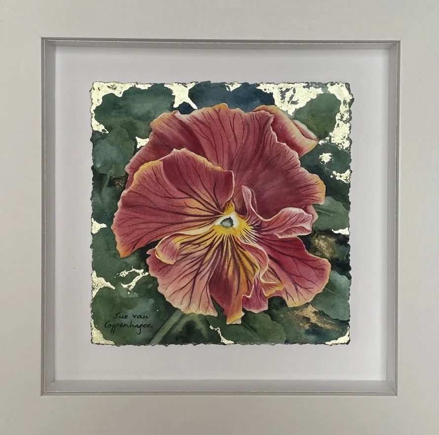 Painting of a plum coloured pansy on a green background with gold leaf, framed in an off white wooden frame