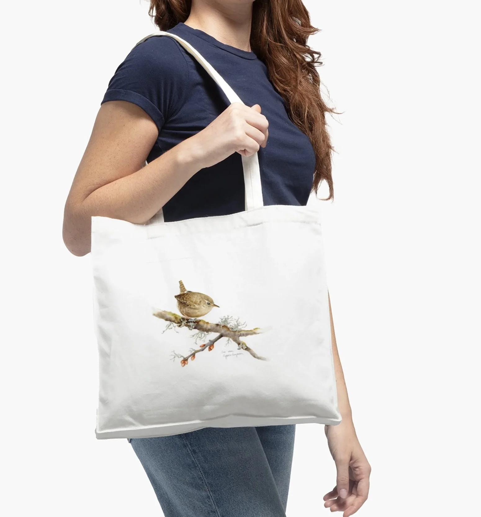 White cotton tote bag with image of a wren on a branch with lichens, worn over the shoulder of a woman dressed in blue