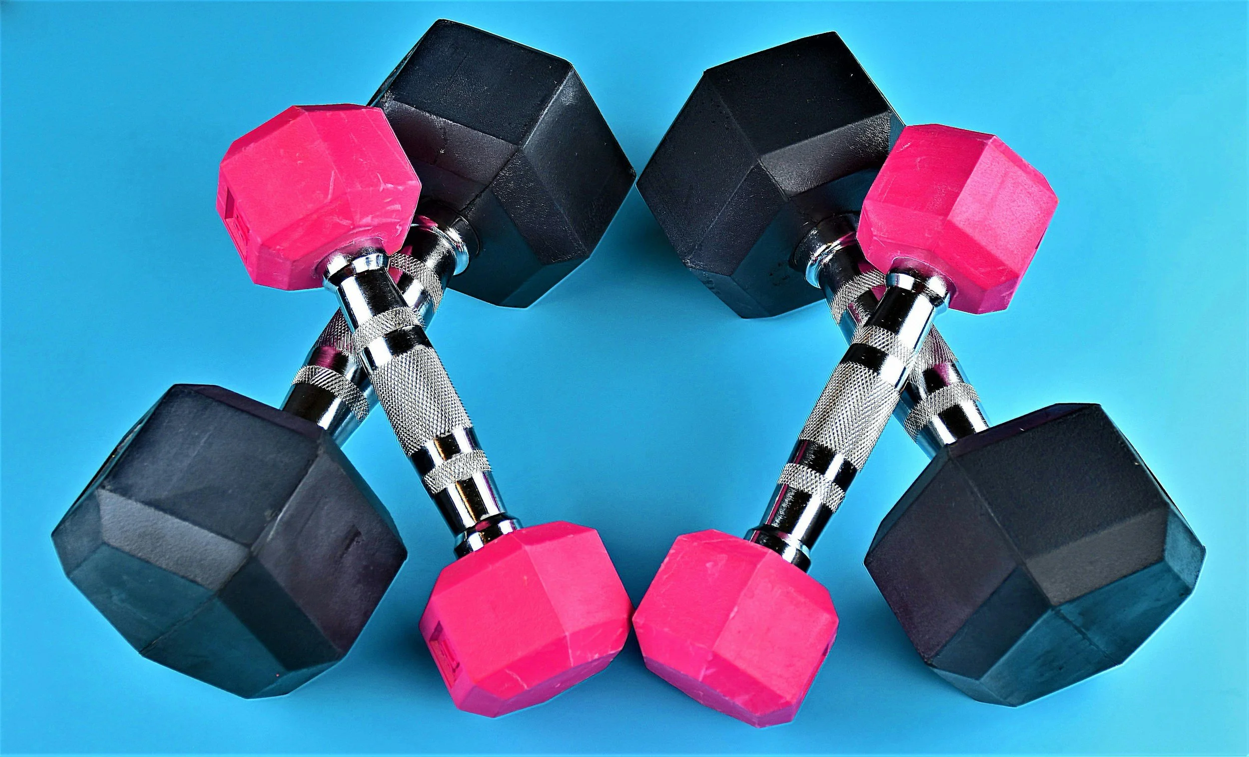 Two adjustable dumbbells with black weights, pink ends, and silver handles on a blue background.