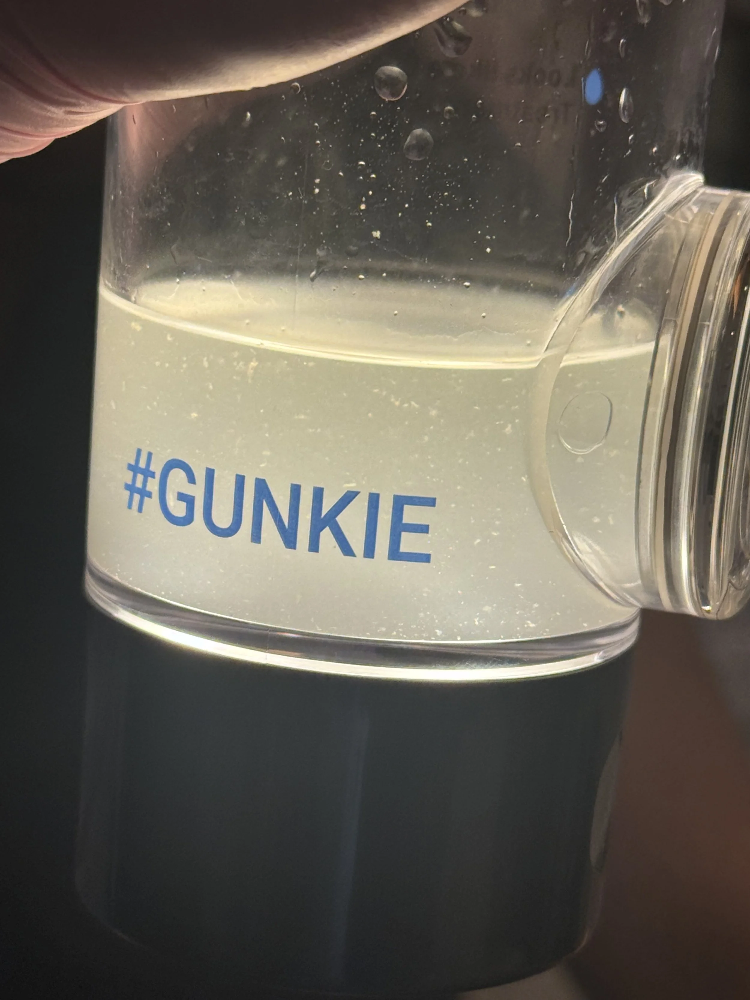 A close-up of a clear plastic container with bubbles inside and the hashtag '#GUNKIE' printed on it.