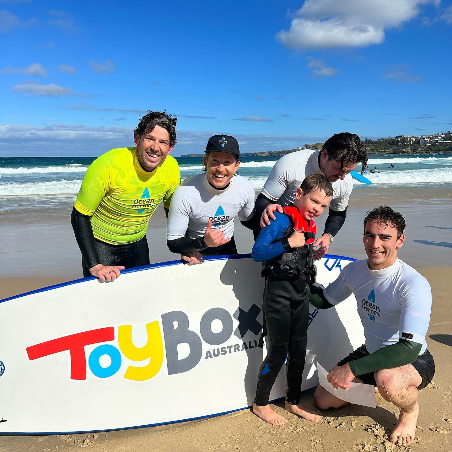 4 surfers with young child at the beach with surfboard