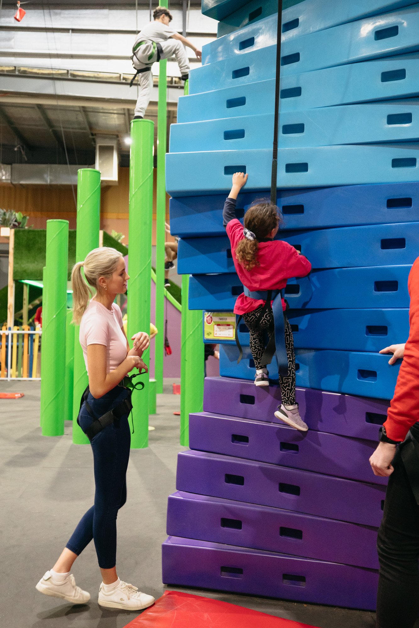 woman helping child climb a wall at adventure centre