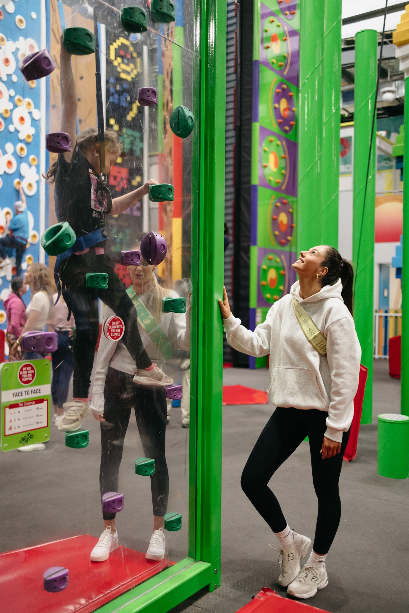 2 women helping child climb colourful rockwall