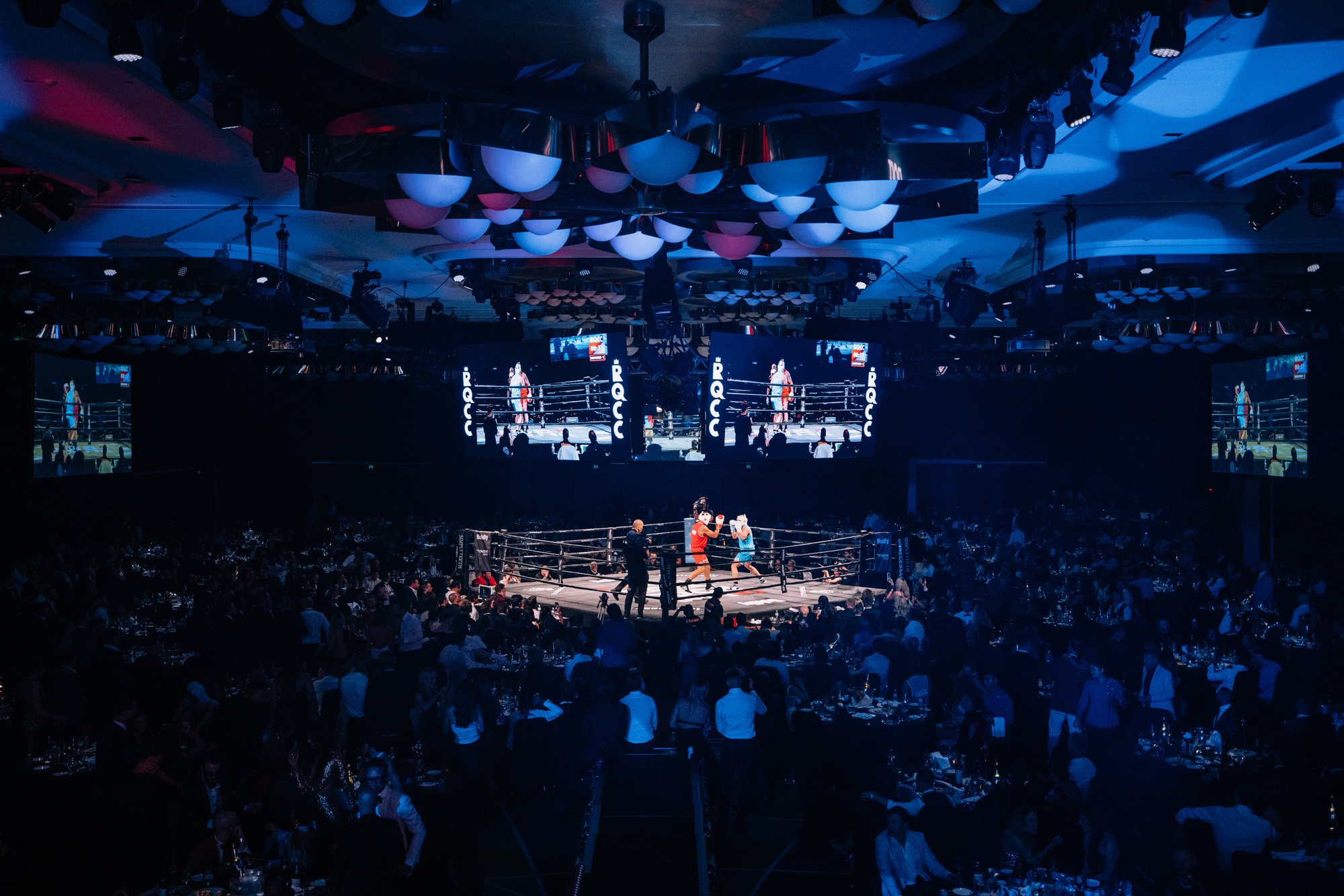 a ballroom with boxing ring in the middle under lights