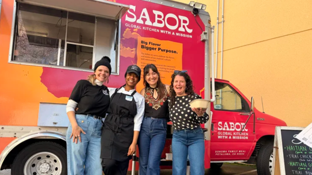 Four SFM employees pose in front of the SABOR food truck smiling with their arms around each other.