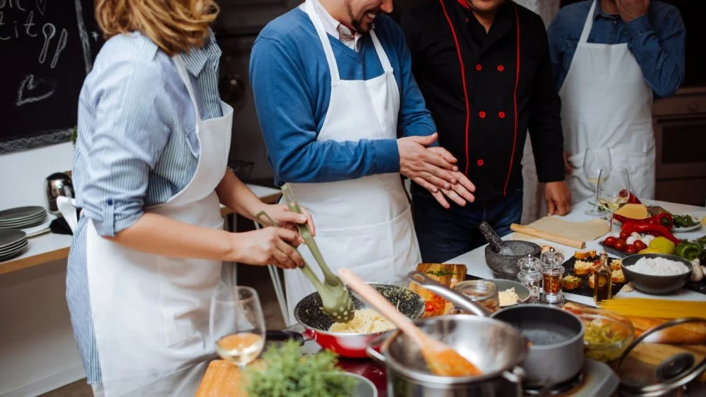 A couple are given instructions by a chef while they stir food in a pan and chop ingredients..jpg