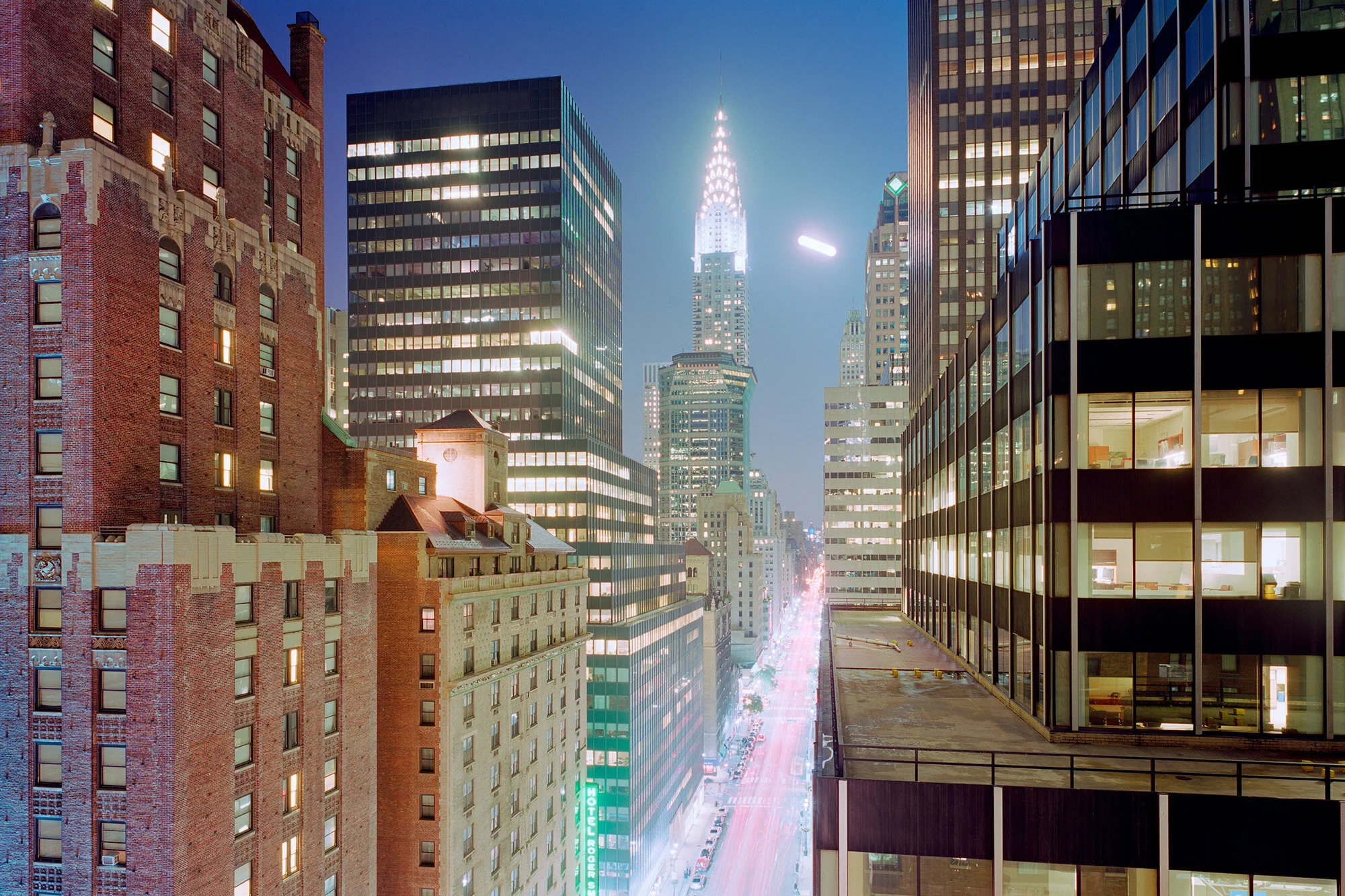 Abendansicht von New York City mit Hochhäusern und der Chrysler Building im Hintergrund, beleuchtete Straßen, Sicht auf einen vertikalen Straßenverkehr mit Lichtspuren.