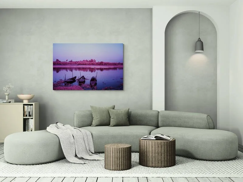 Modernes Wohnzimmer mitgrauem Sofa, Wandkunst mit See und Booten, weiße Wand, kleine Pflanzen und Bücher auf Sessel, zwei kleine runde Tische und eine weiße Teppich.