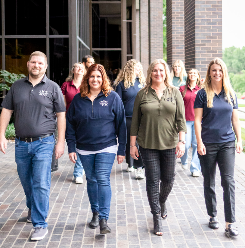 Group of professional people walking outdoors in front of modern building, smiling and dressed in business casual attire.
