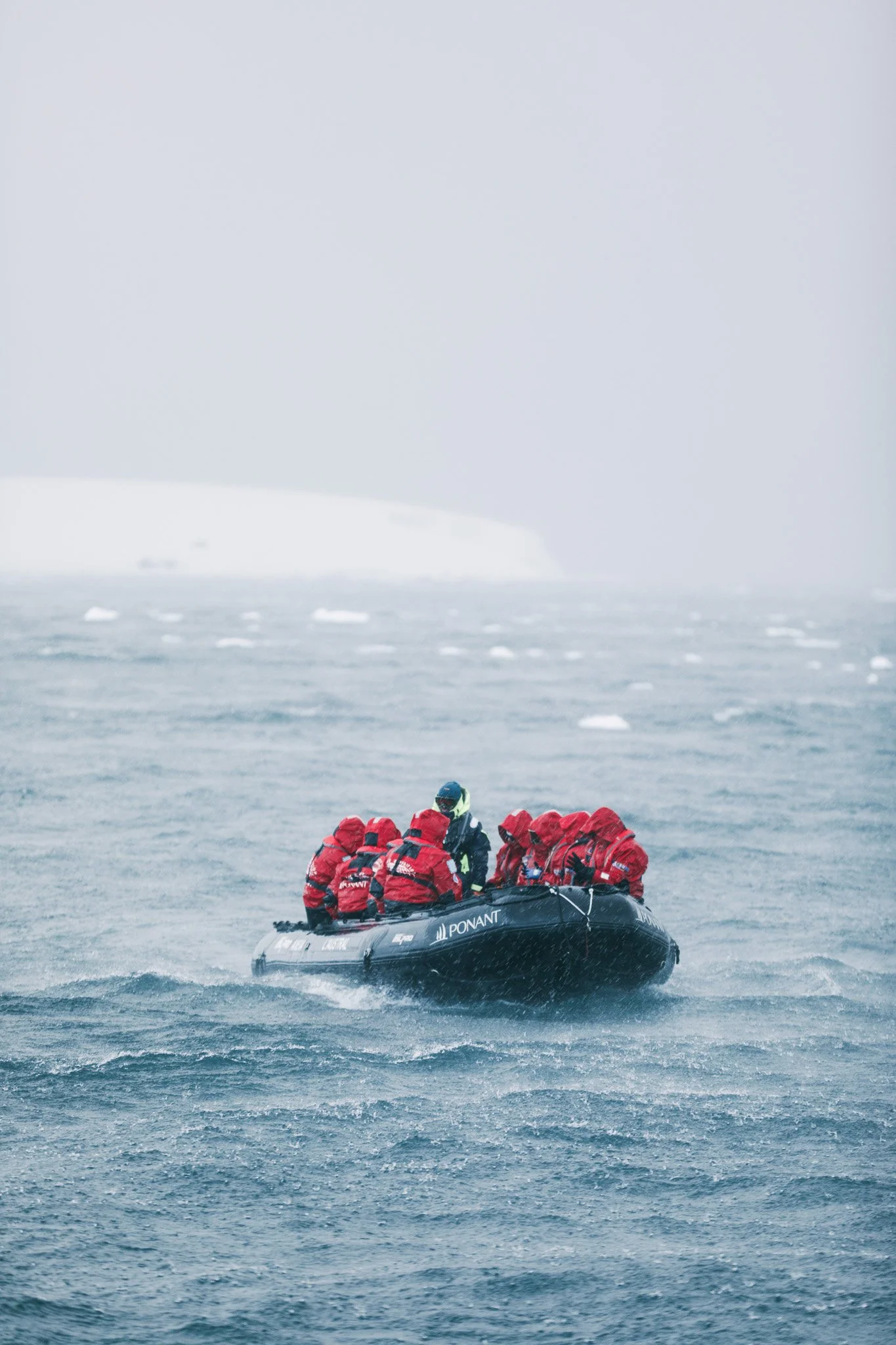 12 guests on a PONANT zodiac ride in the Antarctic Peninsula at Brabant Island. They are in red jackets and everyone had their hood up because it is cold and raining.