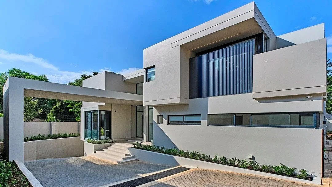 Modern white house with geometric design, large windows, and landscaped driveway