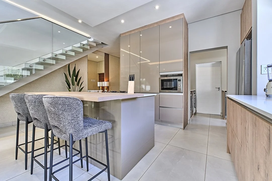 Modern kitchen with a center island, grey bar stools, built-in microwave, and laundry area in the background.