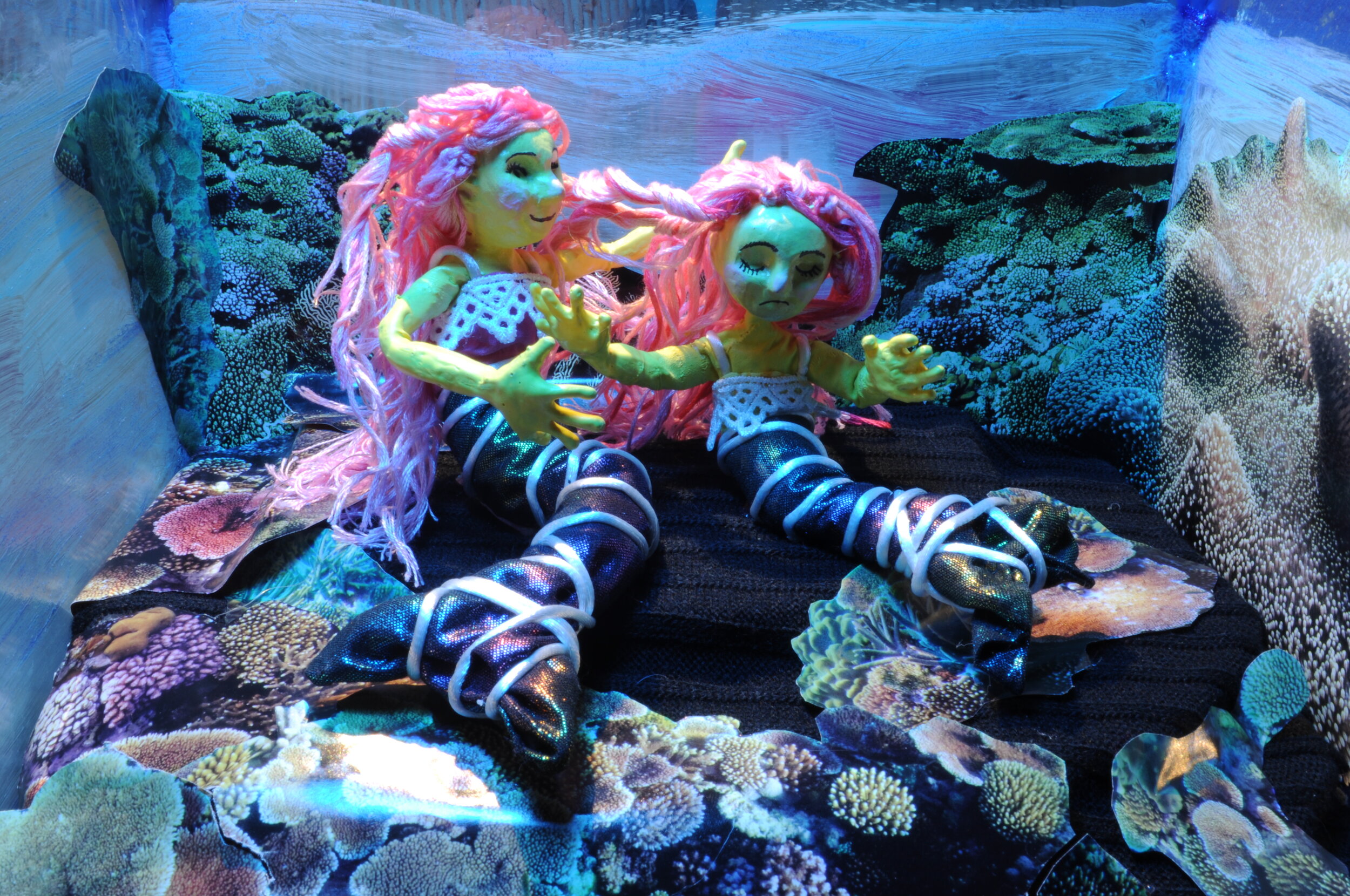  A claymation scene of two pink-haired mermaids in the ocean. 