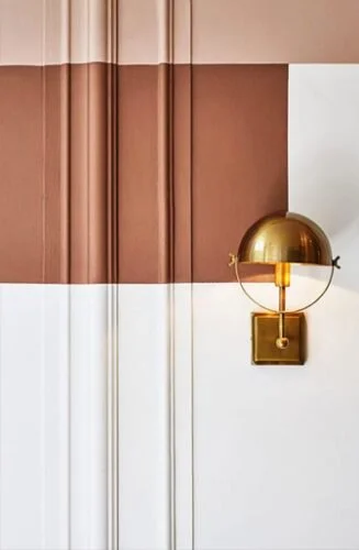 This brass sconce layers beautifully with stripes of warm, earthy red and blush tones. Source Link