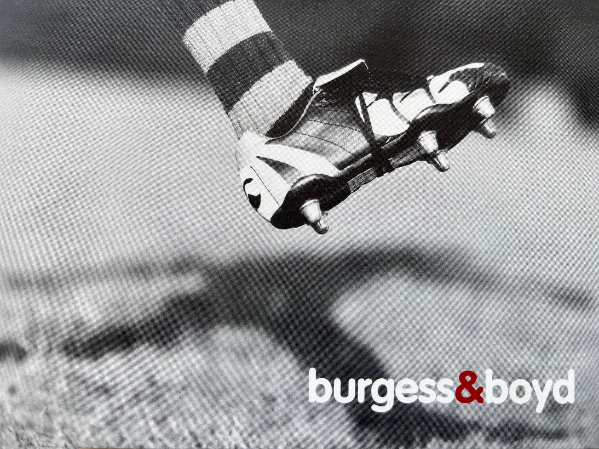 A black and white photograph of a sneaker with a sock visible above it, on a textured surface. Part of a magazine or book cover is visible at the bottom with the words 'burgess & boyd' in white and red text.