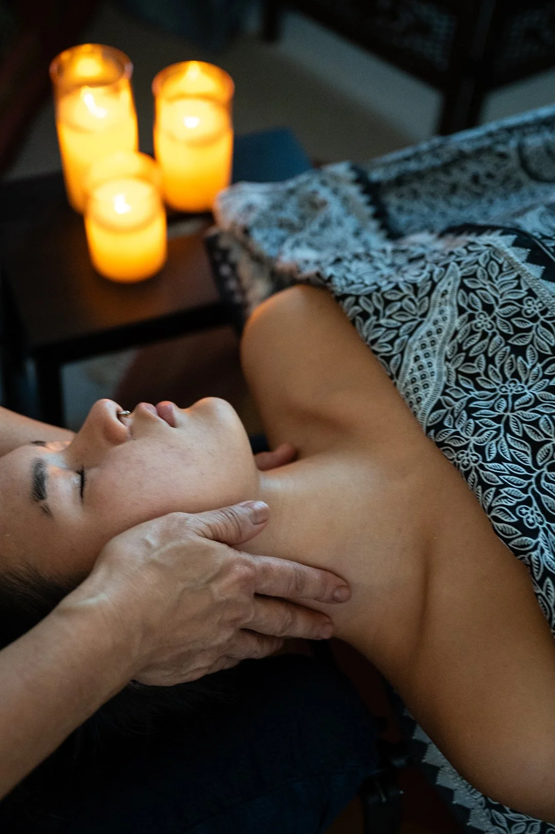 Person receiving a massage or skincare treatment while lying down in a dimly lit room with candles on a side table.