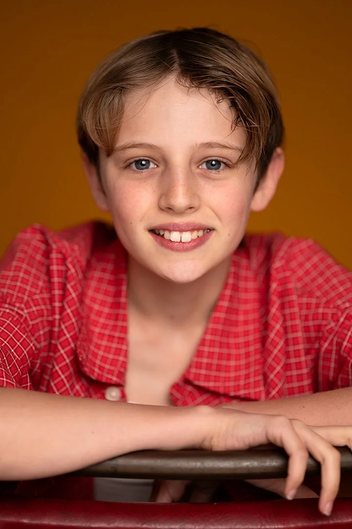 Portrait of a  young boy wearing a red chequered shirt against an orange background smiling . 
