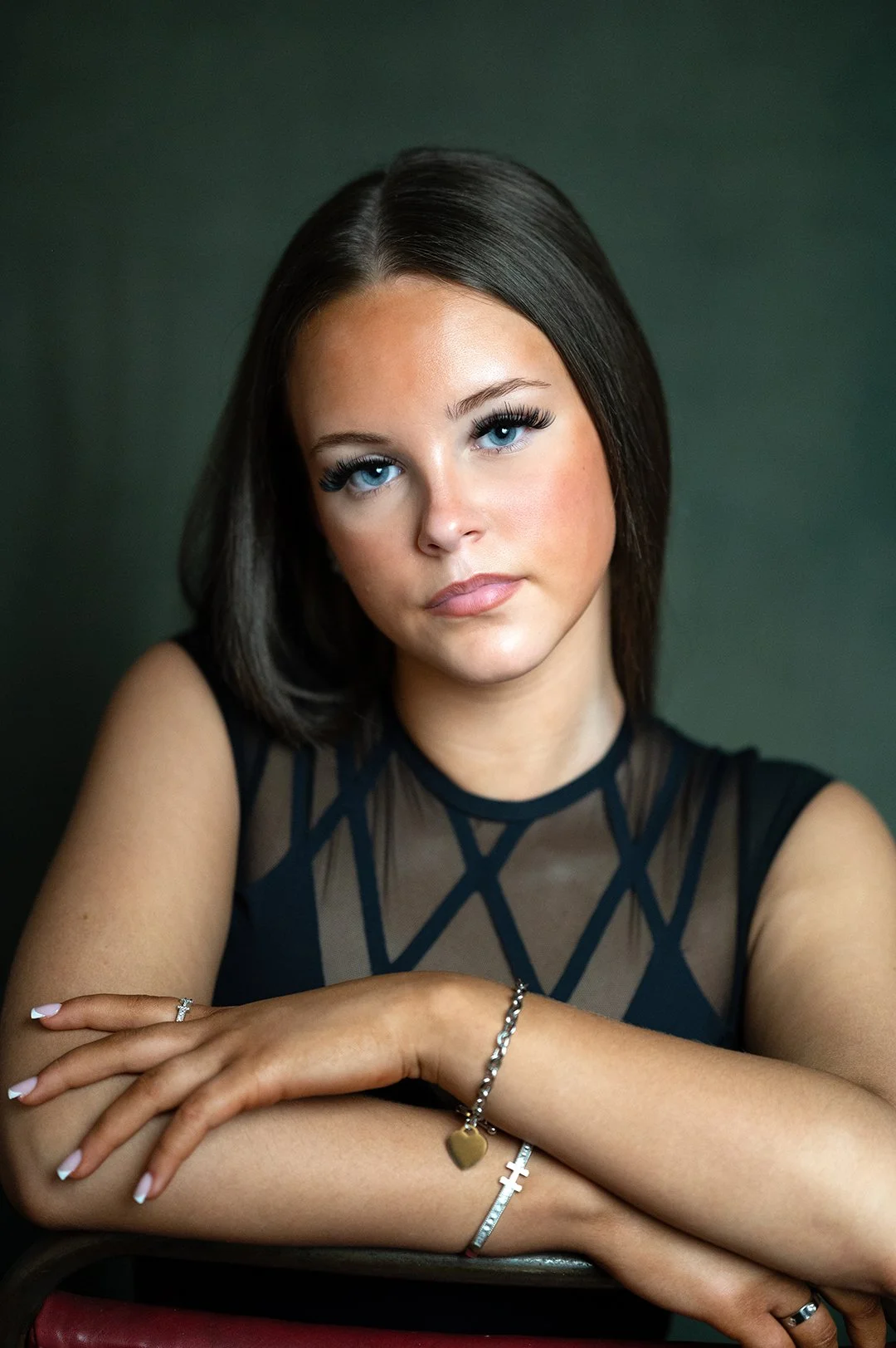 Teenage girl looking at camera with an open expression. She is wearing a black lacey top and has her arms folded in front of her. She has long, straight, dark hair. 