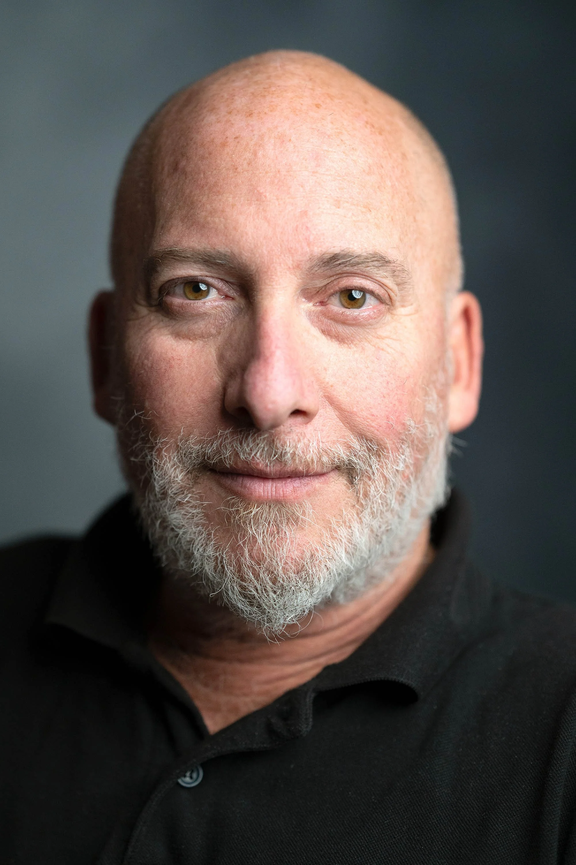 Professional headshot of many wearing black with grey beard in Bristol