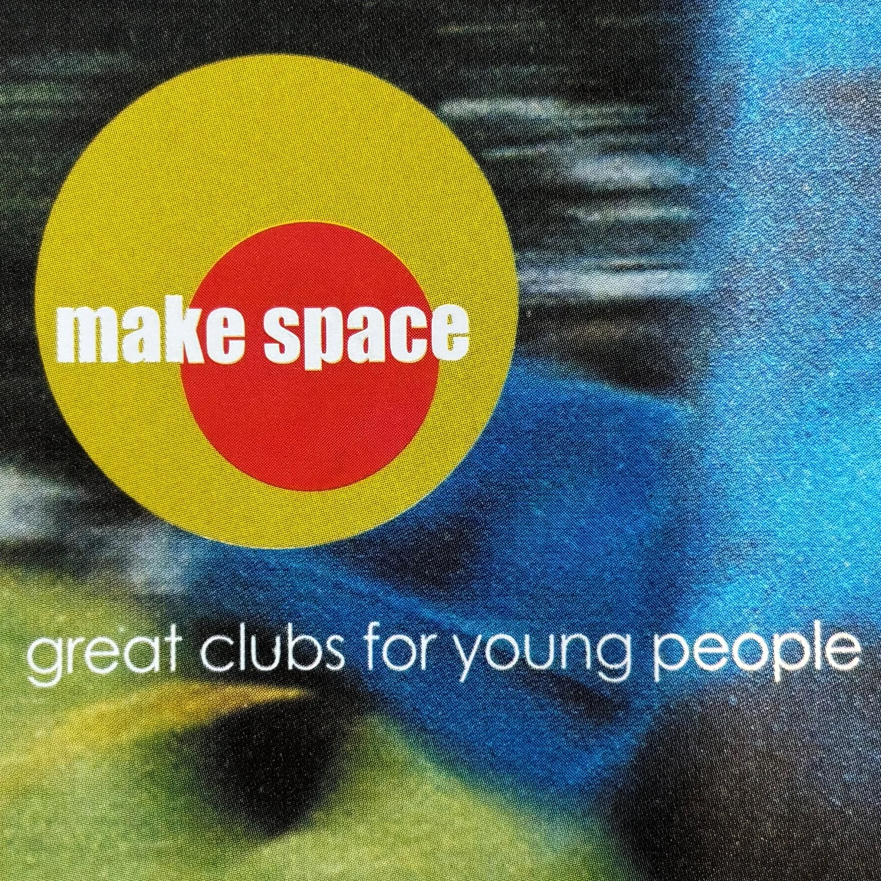 Close-up of a colorful graphic with a yellow circle, a red circle inside it, and the words "make space" in white over the red circle. Part of a blue and green background with some white text is visible.