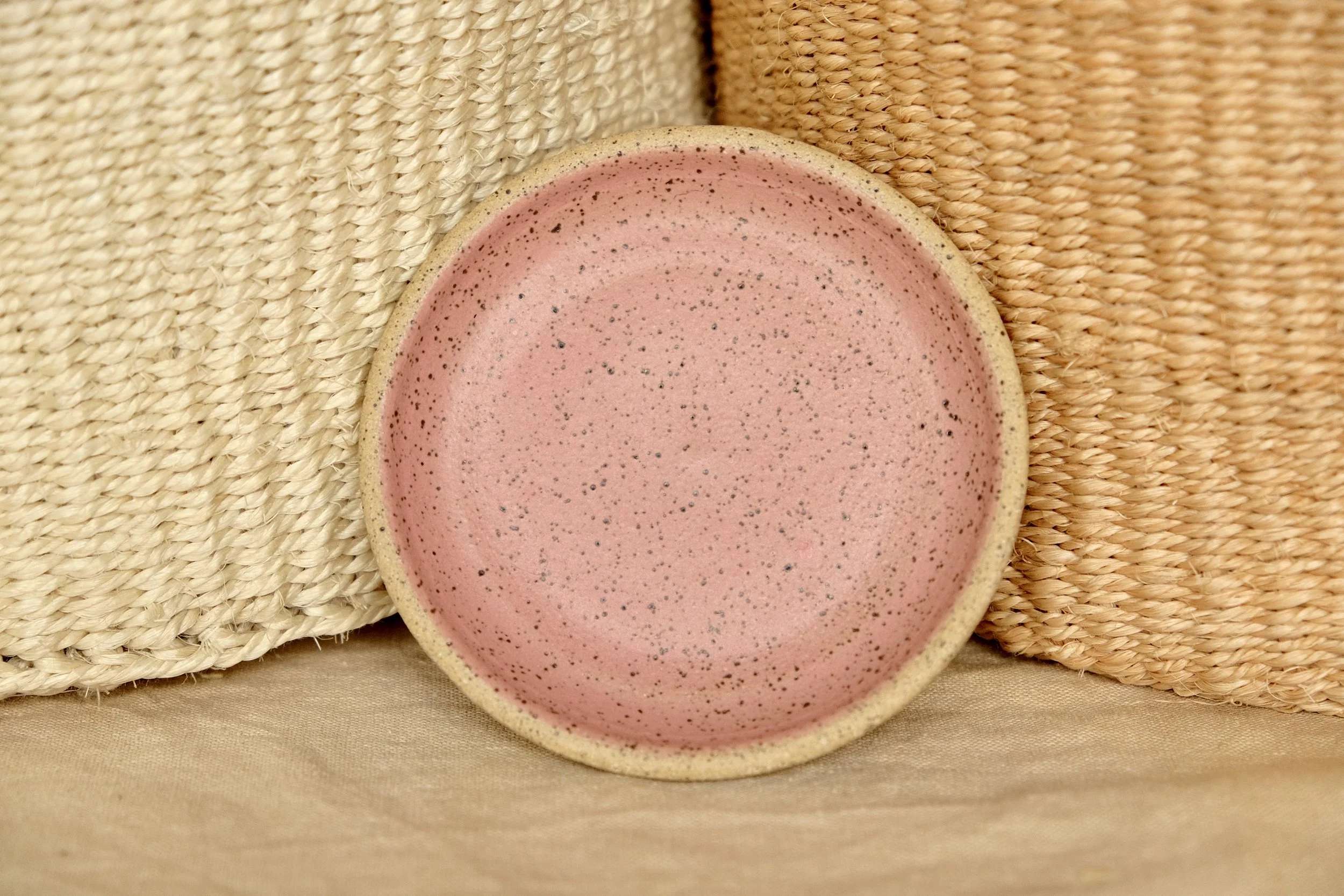 Hand-thrown ceramic ring dish glazed with matte watermelon glaze, resting against warm tablecloth background.