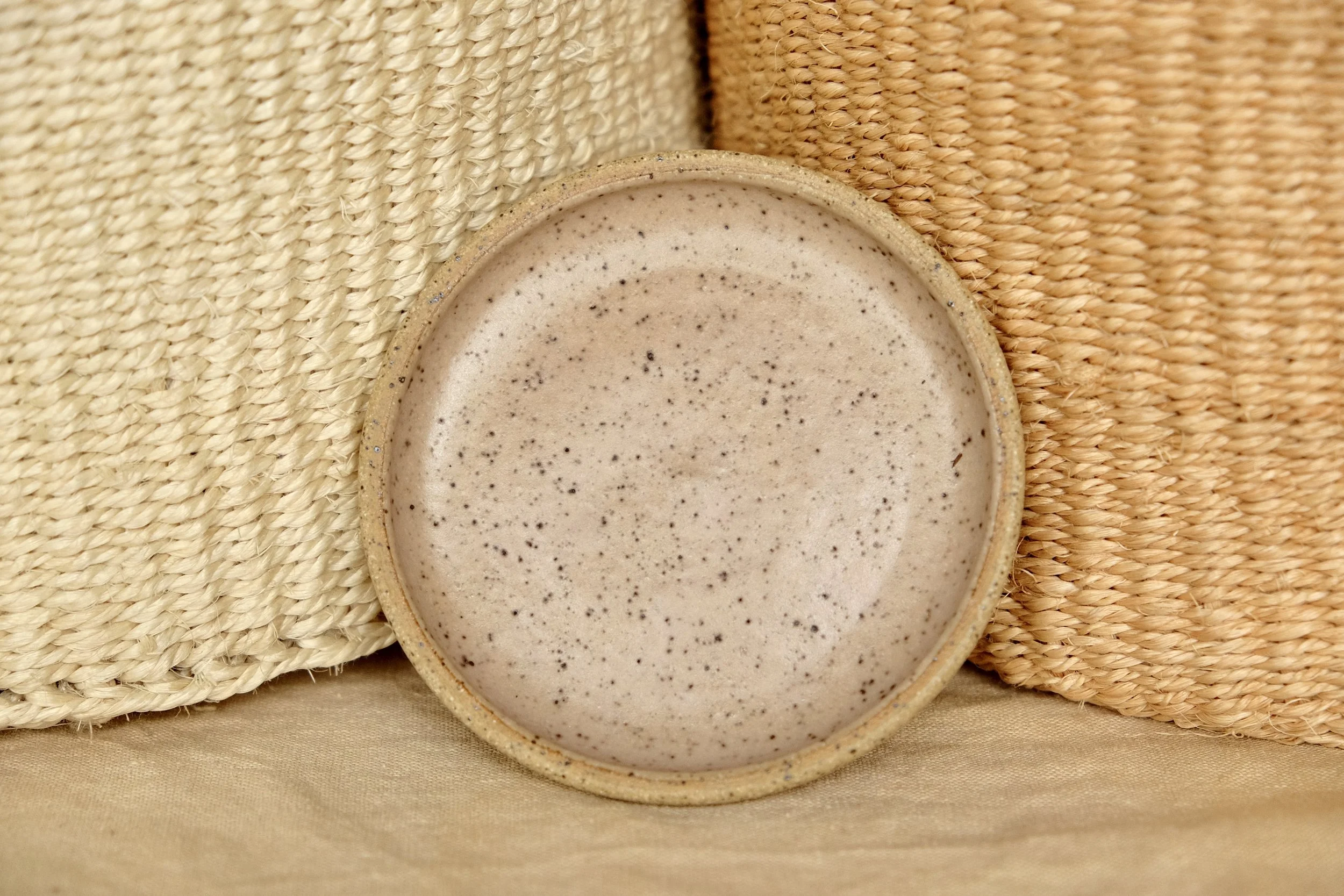 Hand-thrown ceramic ring dish glazed with chai glaze, resting against warm tablecloth background.