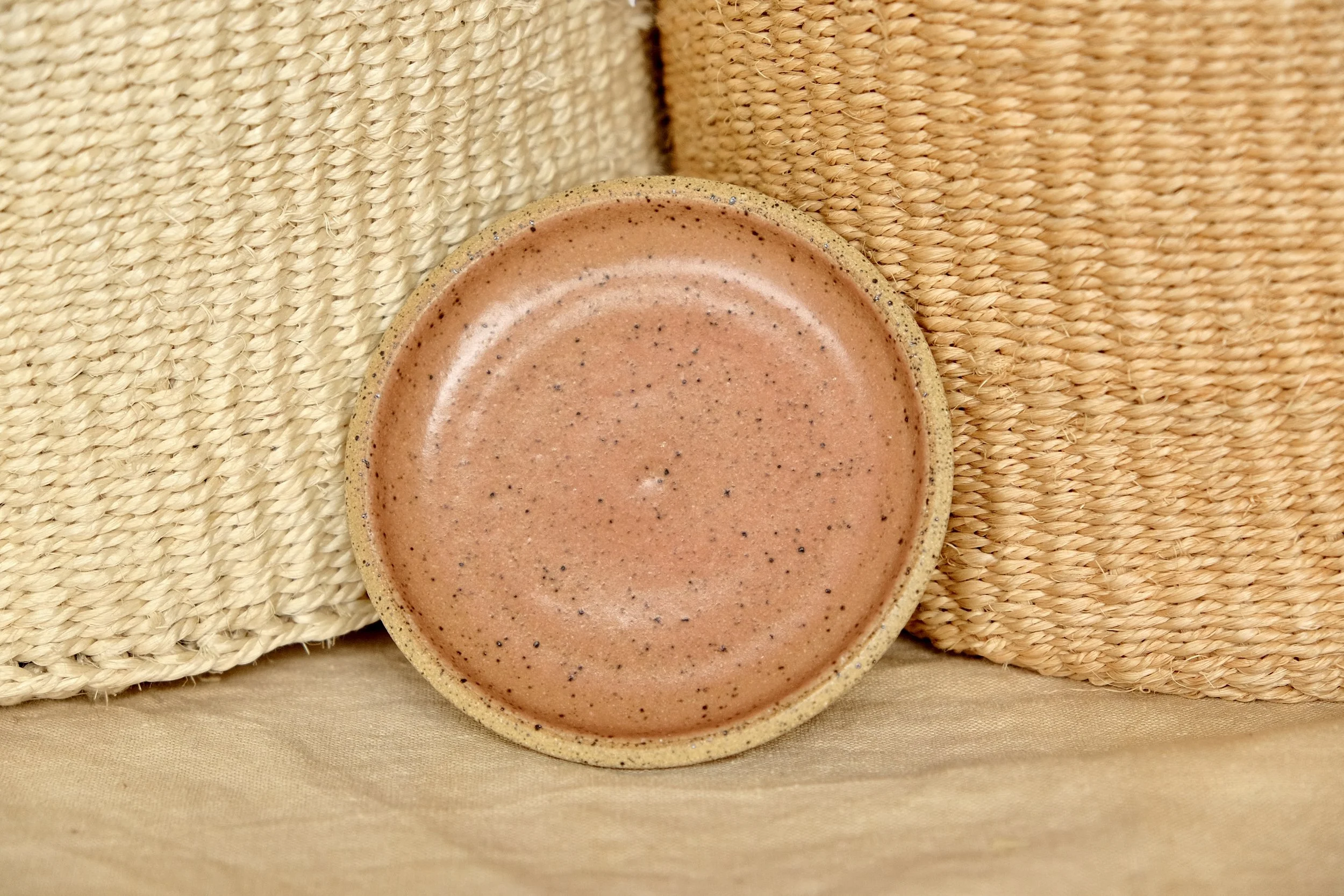 Hand-thrown ceramic ring dish glazed with rose hip glaze, resting against warm tablecloth background.