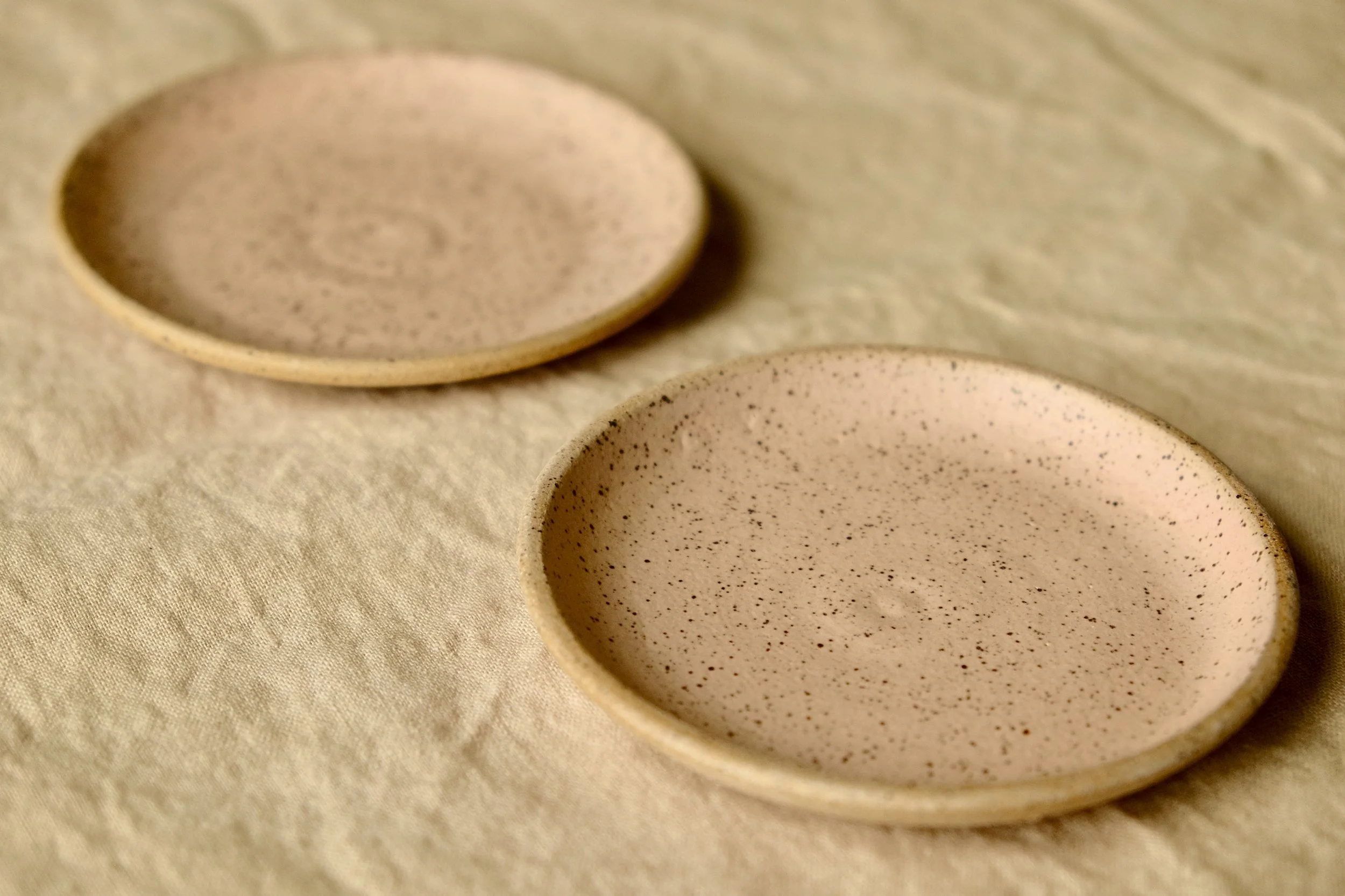 Set of two hand-thrown ceramic ring dishes glazed with matte cherry blossom pink glaze, resting against warm tablecloth background.