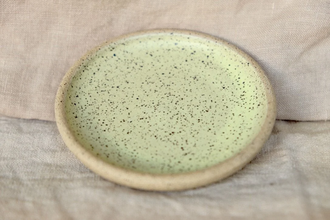 Hand-thrown ceramic ring dish glazed with matte lemon yellow glaze, resting against warm tablecloth background.