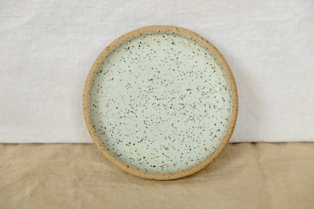 Hand-thrown ceramic ring dish glazed with matte mint glaze, resting against warm tablecloth background.