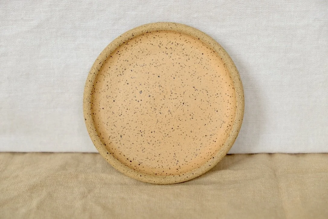 Hand-thrown ceramic ring dish glazed with matte papaya glaze, resting against warm tablecloth background.