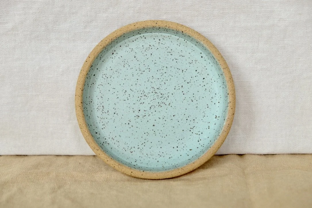 Hand-thrown ceramic ring dish glazed with matte oasis turqoise glaze, resting against warm tablecloth background.