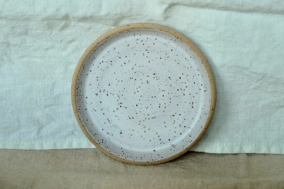 Hand-thrown ceramic ring dish glazed with matte white glaze, resting against warm tablecloth background.