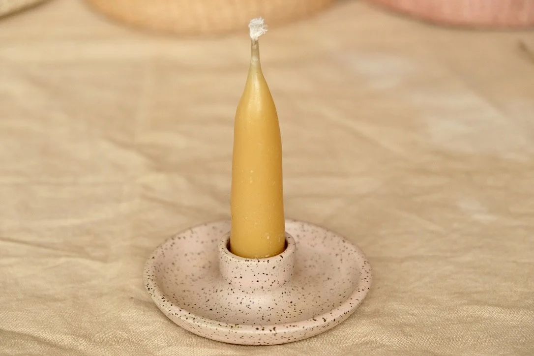 Handmade wheel-thrown ceramic candle holder in light pink glaze sits on a table cloth, with a beeswax candle in the holder..